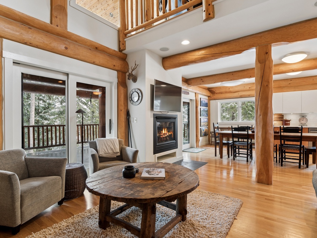 Relax in your mountain retreat's open living space with soaring beamed ceilings, cozy fireplace, and forest views through every window.