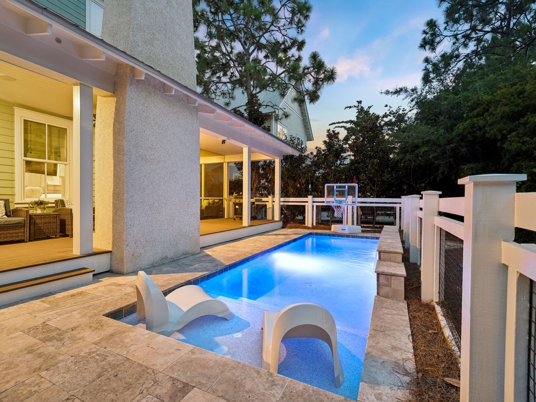 Your private pool awaits, glowing softly in the evening light, complete with poolside loungers and a basketball hoop for playful afternoons. Step out from your bright, welcoming living space onto the deck and slip into complete relaxation.