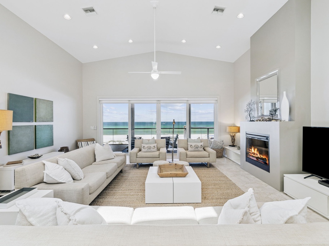 Relax in your stunning beachfront living room, where panoramic ocean views stretch beyond floor-to-ceiling windows and a cozy fireplace awaits.