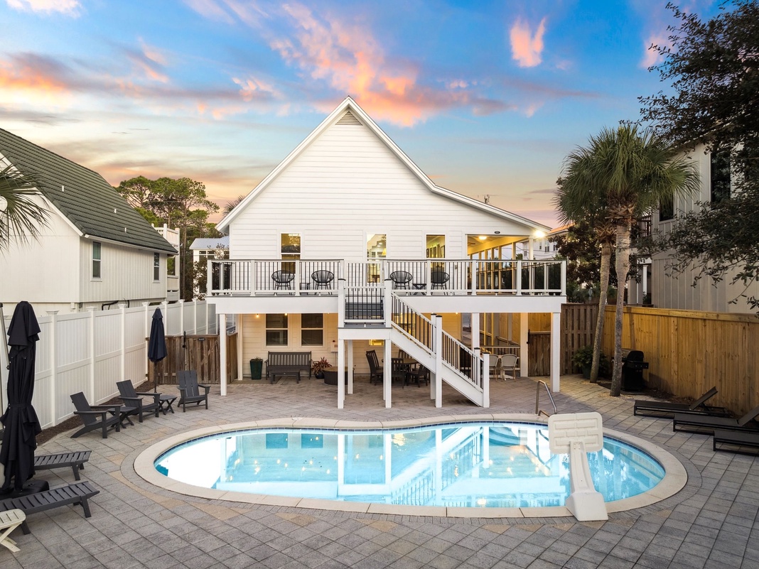 Stunning waterfront property featuring private swimming pool, elevated deck, and panoramic sunset views over palm-lined coastal setting.