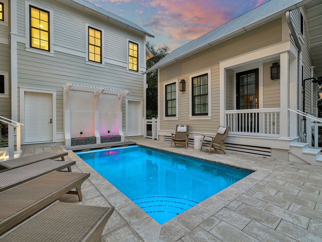 A private courtyard pool glows in the twilight, framed by elegant white columns and surrounded by inviting lounge chairs—perfect for evening swims under pastel skies.