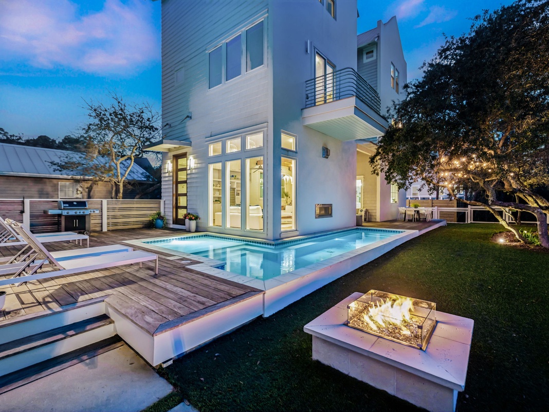 Modern luxury villa with sleek pool deck and elegant outdoor fireplace, perfect for evening gatherings under the stars.
