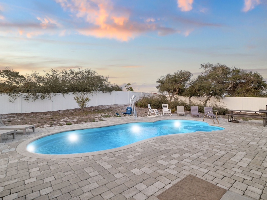 Pool area with evening sky colors in the background, surrounded by paved decking and lounge furniture.