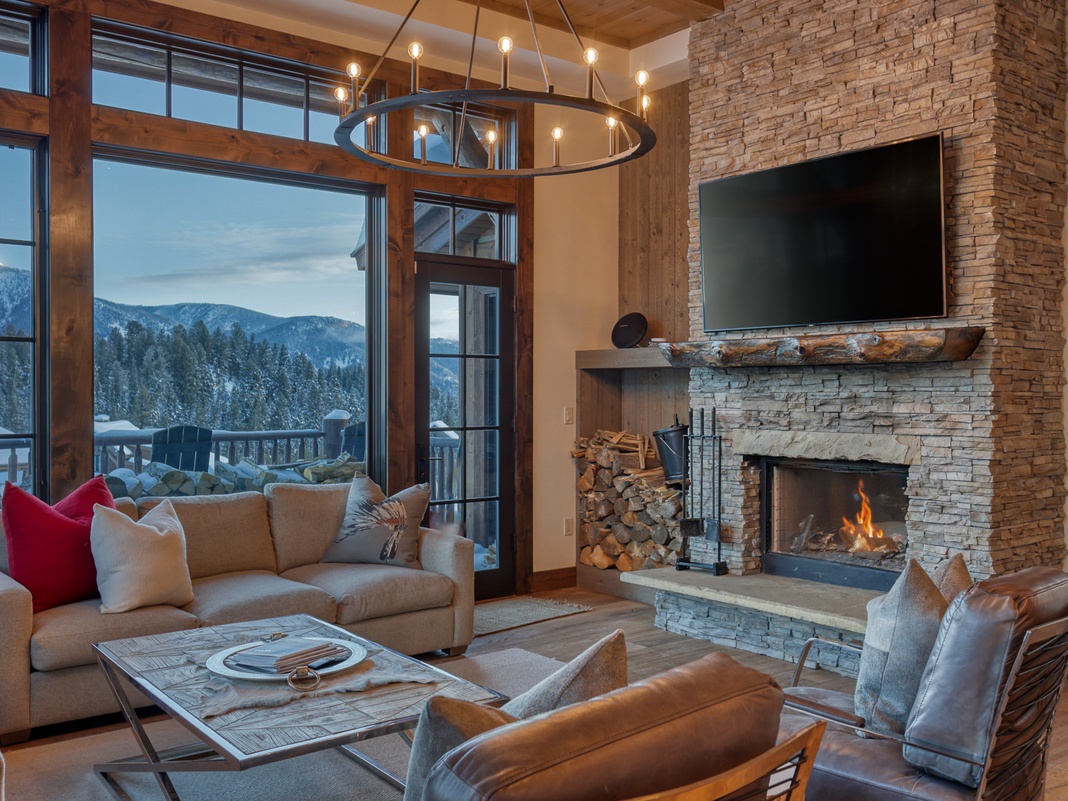 Sink into plush seating by the crackling fireplace while mountain views frame your perfect alpine retreat through floor-to-ceiling windows.