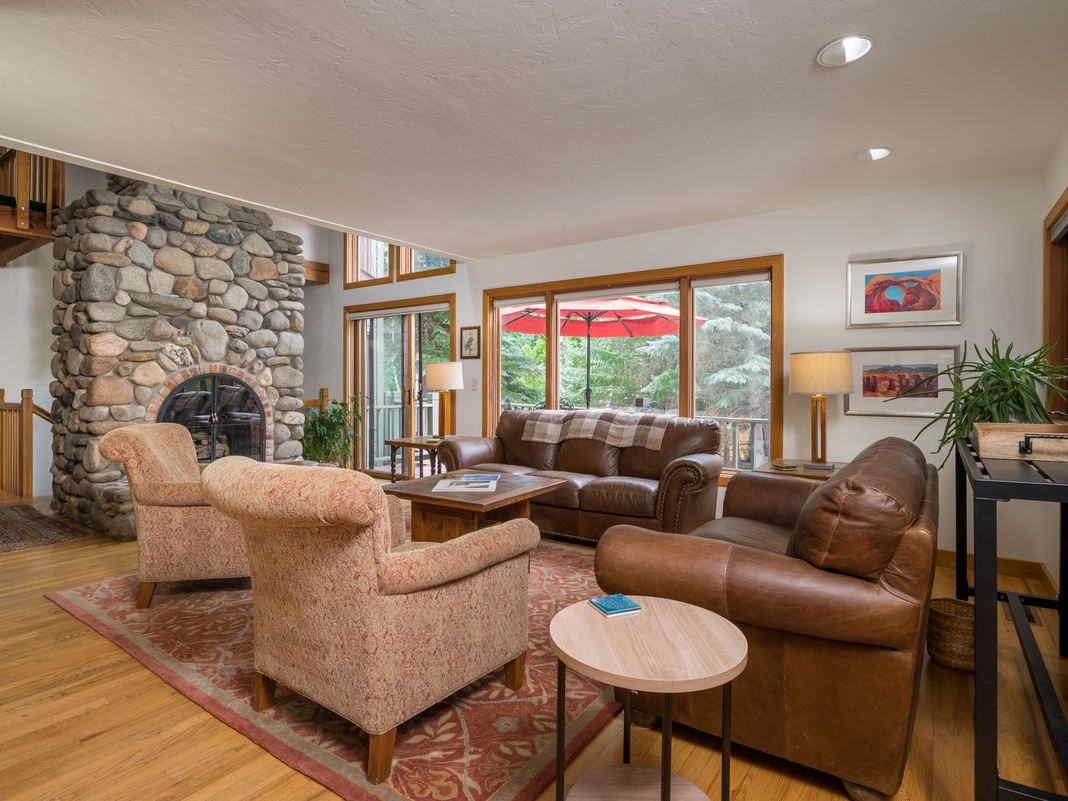 Settle into your cozy living room where a stunning river stone fireplace anchors the space. Rich leather seating and warm wood tones invite you to unwind with views of the surrounding forest through expansive windows.