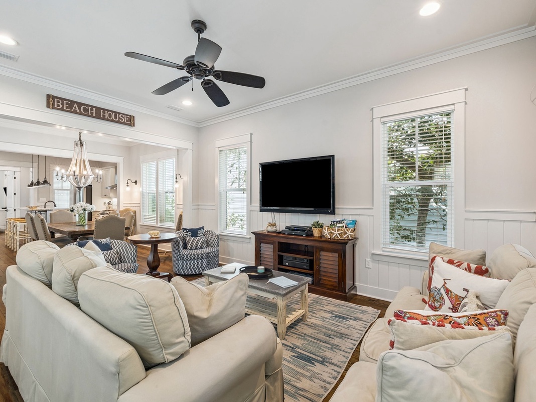 Sink into plush sofas in your bright, airy living space where coastal charm meets modern comfort with ceiling fan breezes and entertainment ready.