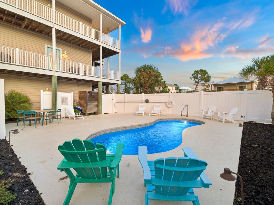 A picturesque coastal property situated in a residential neighborhood, photographed during golden hour beneath a stunning sunset sky, with palm trees dotting the surrounding area.