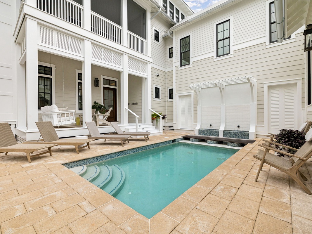 Your private courtyard retreat features a sparkling pool surrounded by elegant loungers and cozy seating, all framed by bright white architecture and warm natural light—perfect for unwinding in style.
