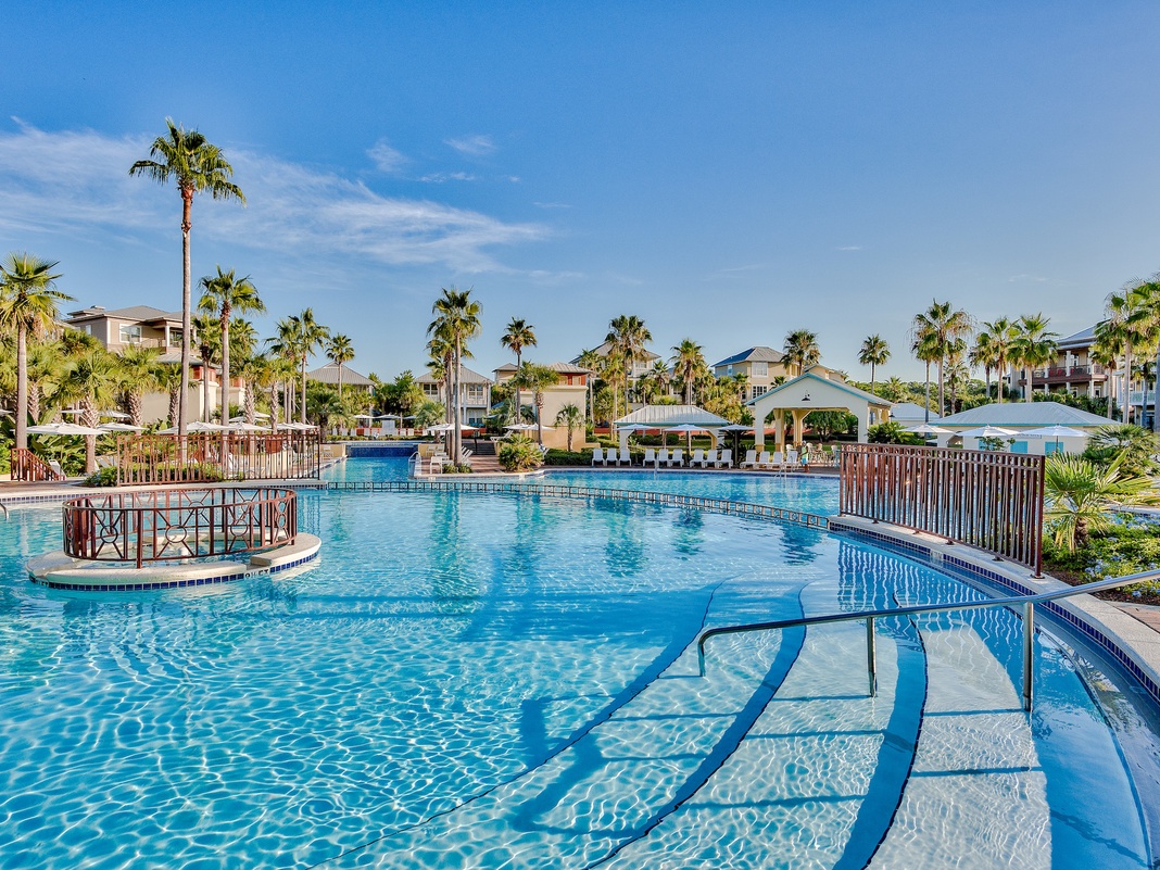 Resort-style swimming pool surrounded by tropical palm trees and vacation homes in a beautiful sunny setting.