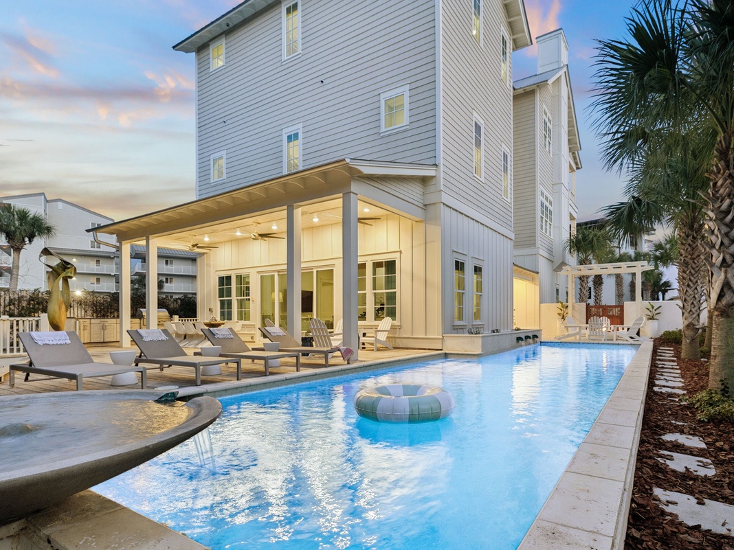 Modern coastal home featuring a private swimming pool and covered patio area surrounded by tropical palm trees.