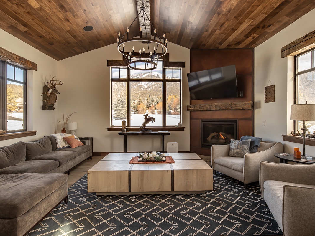 Cozy up in your rustic-chic living room with vaulted wood ceilings, where plush seating surrounds a warm fireplace and snowy mountain views frame perfect winter evenings.