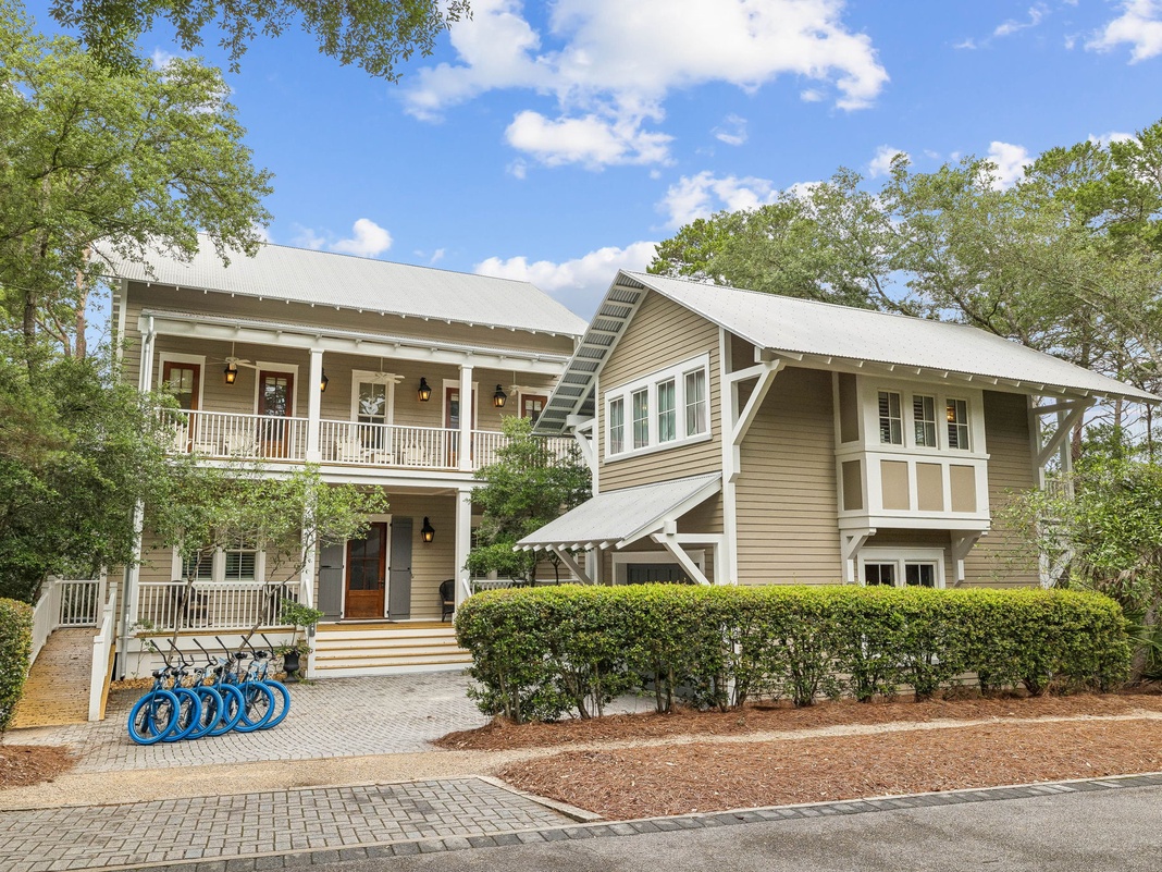 A charming two-story coastal home with double-wrap porches, bicycle parking, and lush landscaping welcomes guests to a peaceful neighborhood retreat.