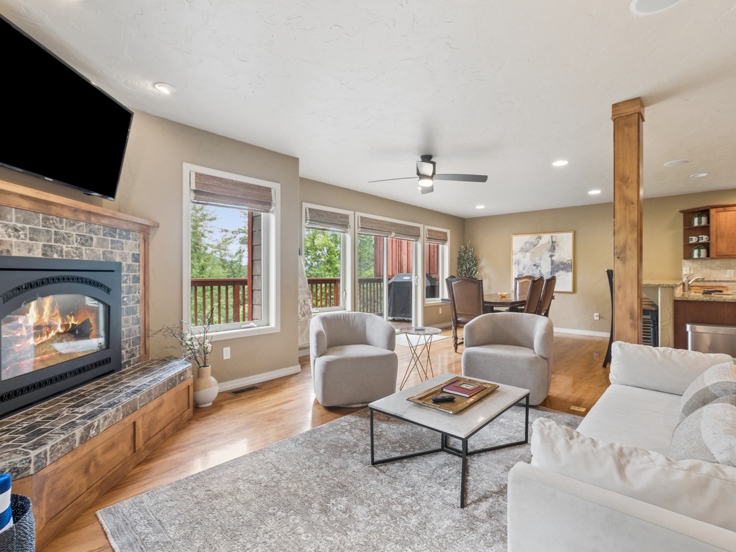 Unwind in your spacious living room featuring a cozy stone fireplace, plush seating, and expansive windows framing lush outdoor views—your perfect mountain retreat awaits.