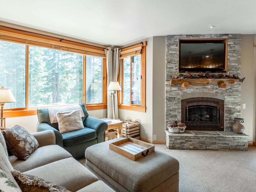 Curl up in this cozy living room where a stone fireplace and plush seating invite you to relax while forest views frame your mountain escape.
