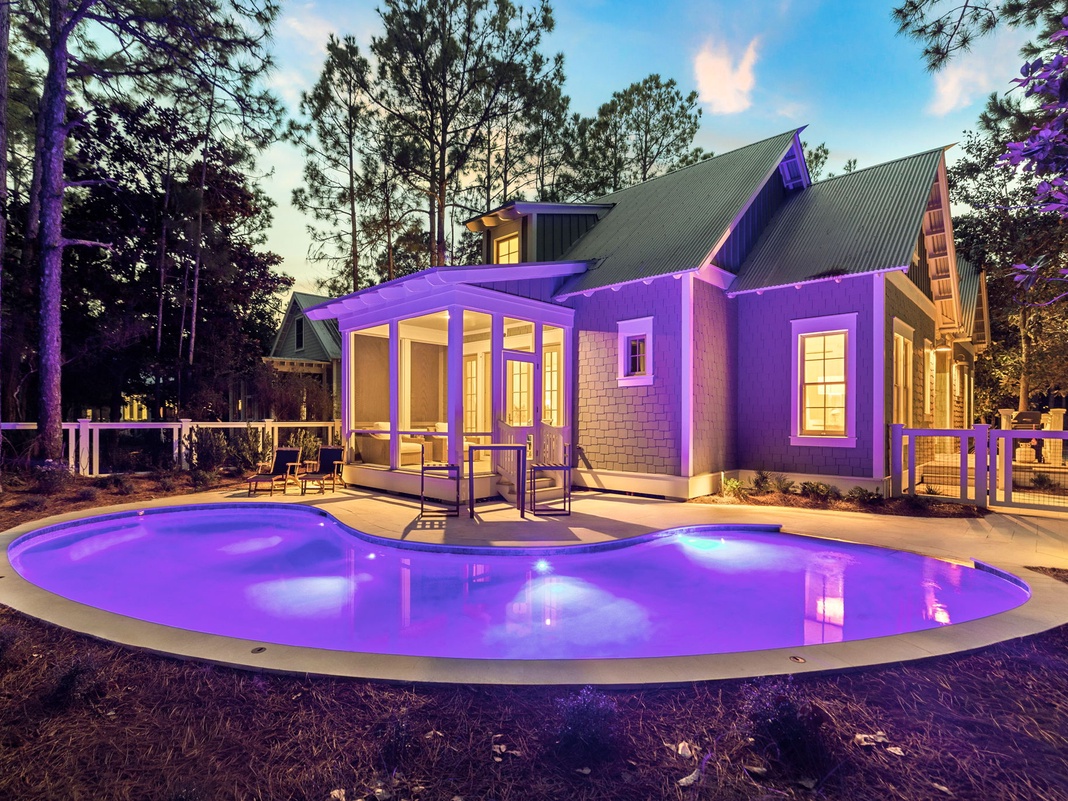 Modern vacation home nestled among towering pines features stunning purple LED lighting and curved pool creating magical evening ambiance.