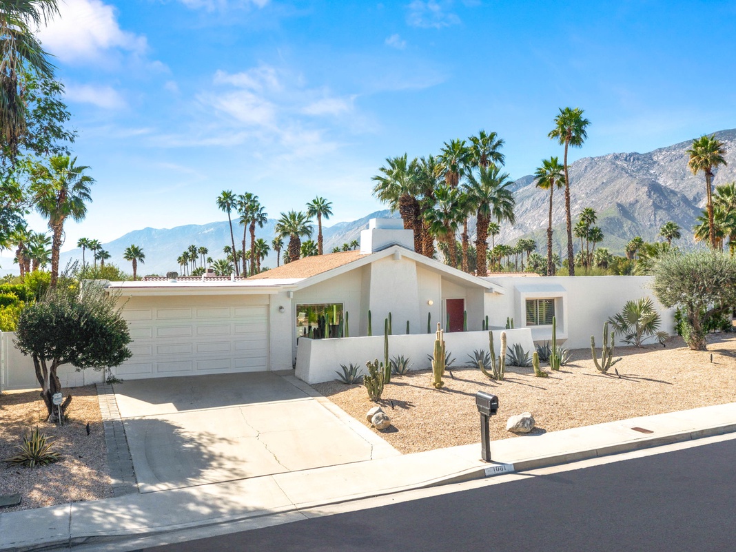 Modern desert retreat nestled beneath towering palms and mountain peaks, featuring clean lines and desert landscaping in a tranquil neighborhood setting.