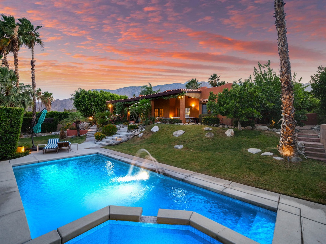 Stunning desert retreat captured beneath a vibrant sunset sky, featuring a sparkling pool surrounded by lush landscaping, palm trees, and mountain views—perfect for a serene getaway.