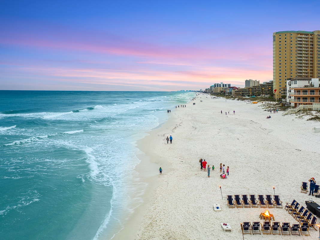 Pristine white sand beach with crystal-clear turquoise waters stretches along the coastline, featuring beachfront high-rise buildings and vacation rentals.