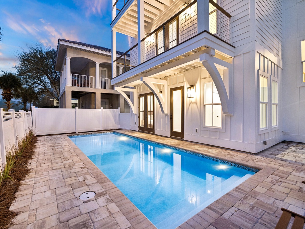Elegant white coastal home featuring a private pool surrounded by stone pavers, tropical landscaping, and covered outdoor living spaces.