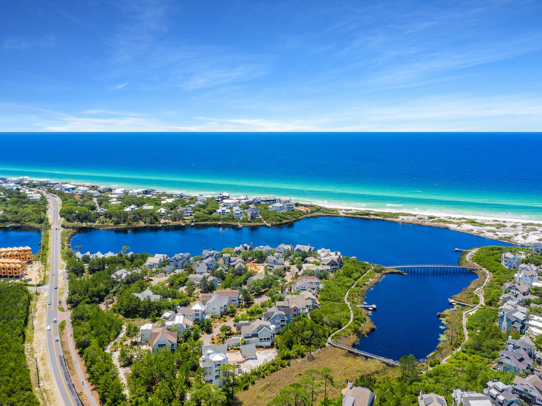 Stunning aerial view of a pristine coastal community featuring emerald waters, white sand beaches, and charming lakefront homes nestled among lush greenery.