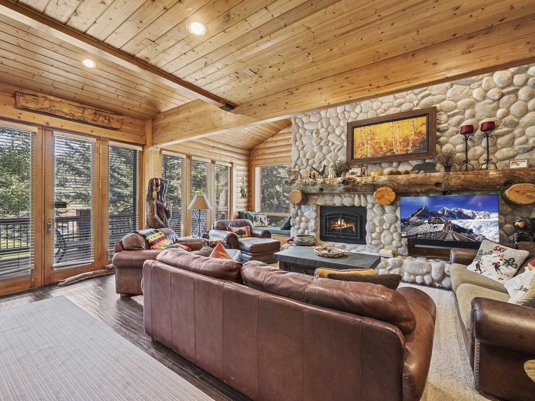 Settle into plush leather seating as the stone fireplace crackles and natural light streams through floor-to-ceiling windows. Your cabin retreat blends rustic charm with cozy comfort—perfect for unwinding after mountain adventures.