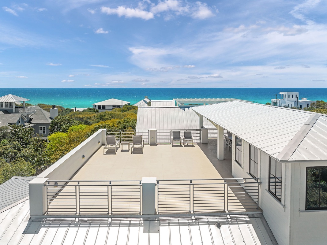 A rooftop terrace overlooks turquoise waters and coastal dunes, offering an elevated outdoor retreat in a serene beachside setting.