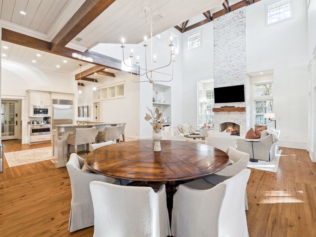 Step into your elegant open-concept haven where soaring ceilings and rich wood beams frame intimate dining moments by the cozy fireplace.