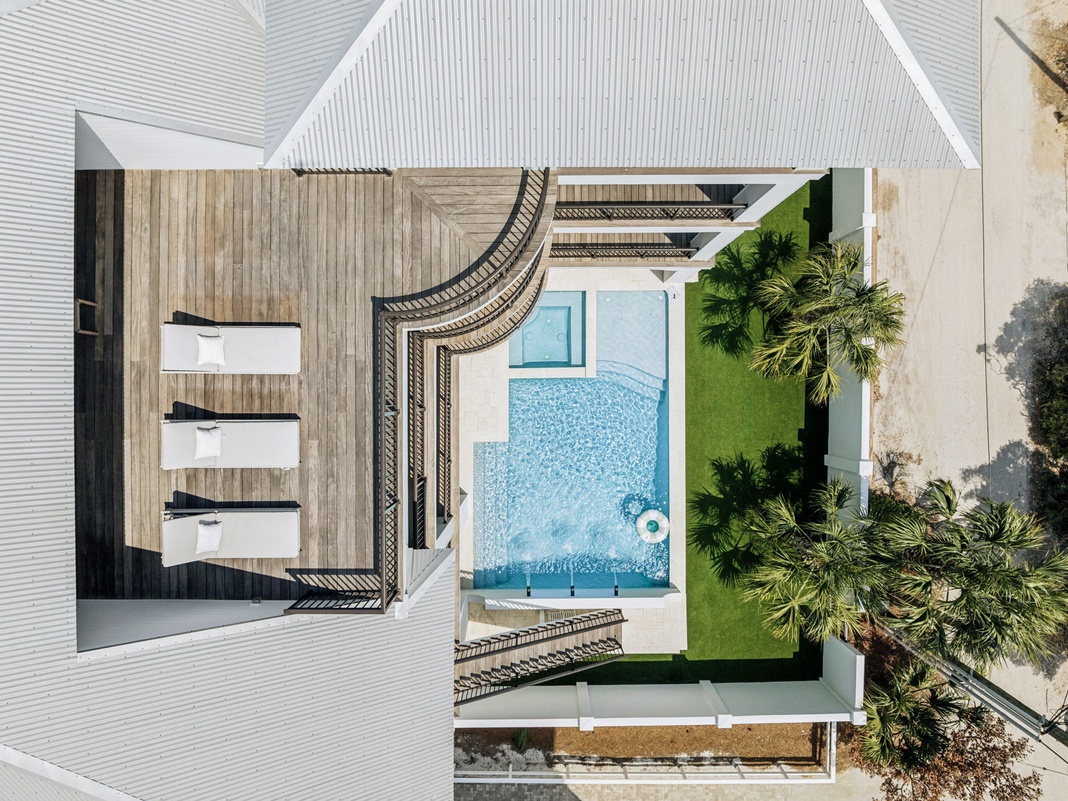 Aerial view showcasing the property's stunning pool and lush tropical landscaping with palm trees and manicured lawn areas.