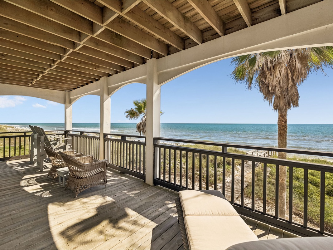A covered beachfront patio offers stunning Gulf views framed by swaying palms. Relax in your lounge chair as gentle sea breezes drift through this shaded outdoor retreat.