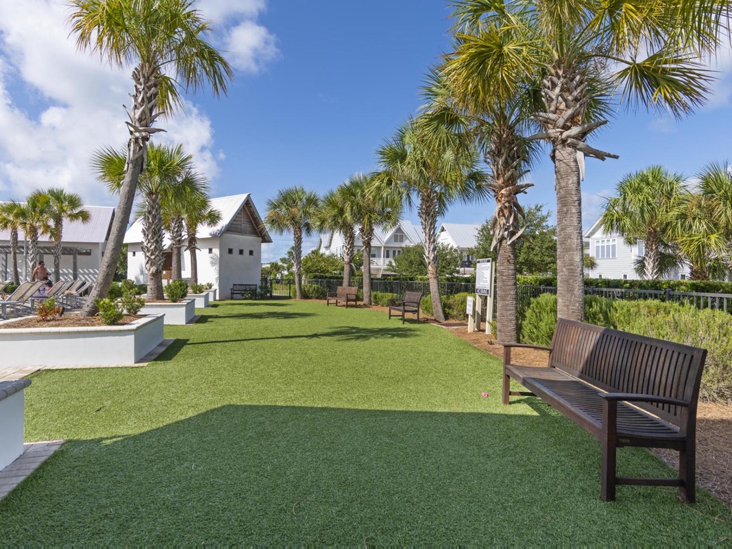 Tropical resort grounds feature palm-lined lawns, wooden benches, and poolside lounging areas beneath sunny Florida skies.