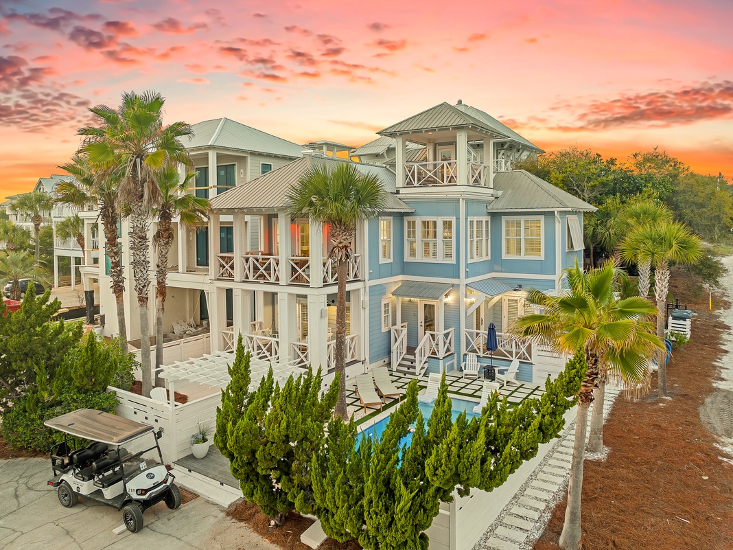 Stunning coastal home with turquoise siding and tropical palms, captured during a spectacular sunset over the neighborhood.