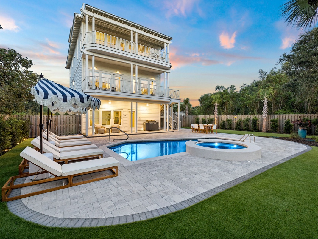 Stunning coastal-style property featuring a sparkling pool and separate hot tub, surrounded by manicured lawns, palm trees, and spacious balconies overlooking the serene backyard oasis.