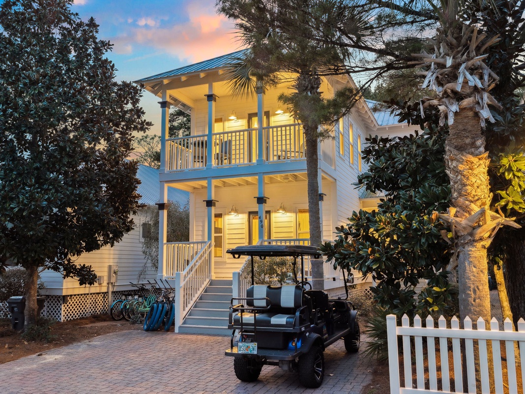 Charming coastal cottage with warm evening lighting creates a welcoming arrival, complete with palm trees and golf cart for easy island exploration.