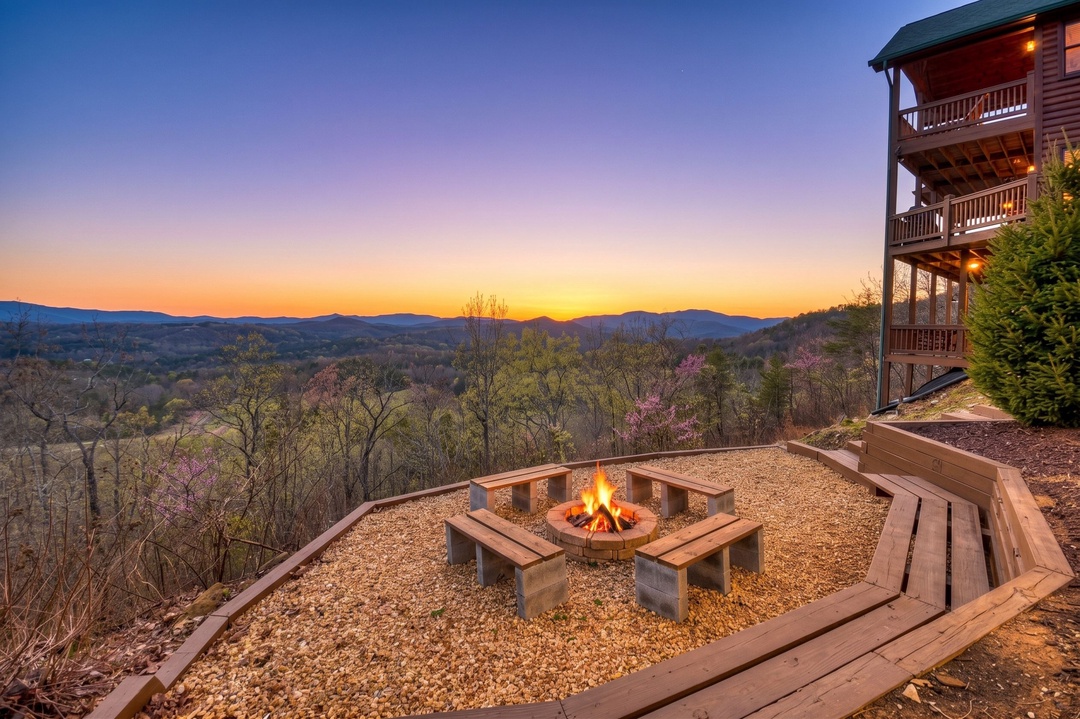 This mountain property features a multi-level wooden cabin and an outdoor fire pit area set against sweeping mountain ranges at sunset.