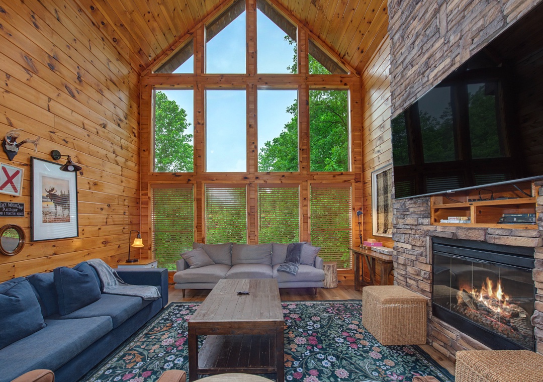 Your living room features soaring windows framing lush forest views, cozy sofas to sink into, and a crackling stone fireplace that sets the perfect mood for mountain evenings.