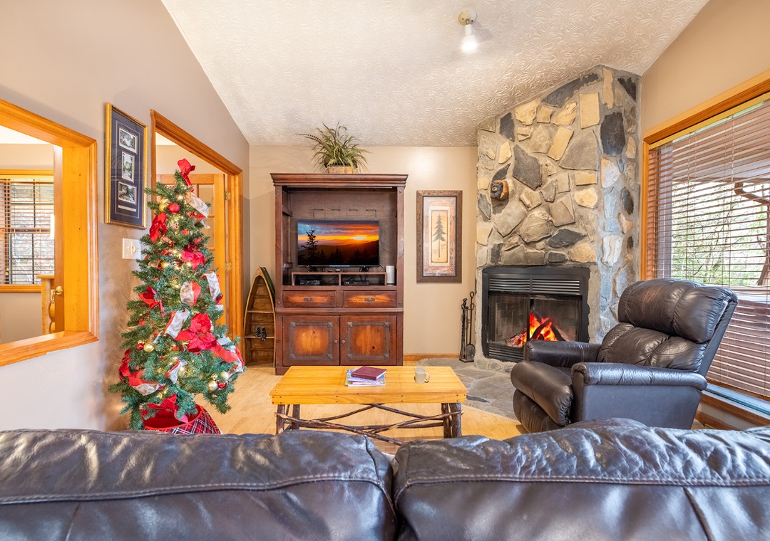 Cozy up by the crackling stone fireplace in your inviting living room, where leather seating and warm wood create perfect holiday memories.