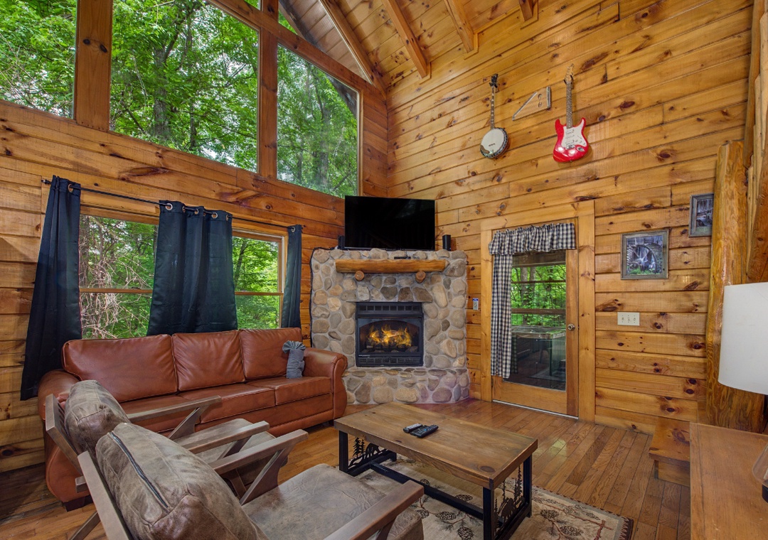 Unwind in this cozy living room where warm wood surrounds you, a stone fireplace crackles with welcoming heat, and floor-to-ceiling windows frame lush forest views. Your peaceful retreat awaits.