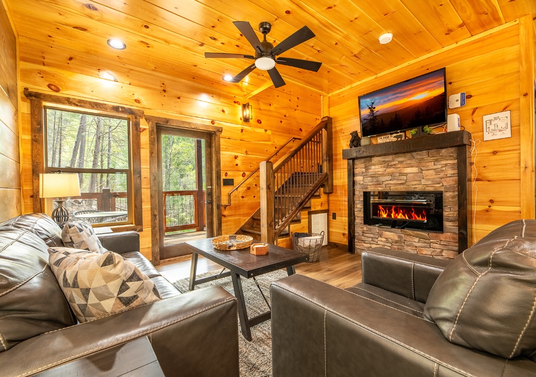Cozy up in your rustic living room with warm wood walls, crackling fireplace, and forest views through picture windows.