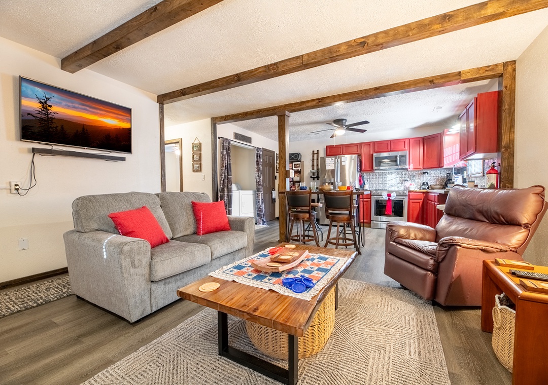 Cozy up in your mountain lodge living room with rustic beams, plush seating, and a vibrant red kitchen ready for cooking adventures.