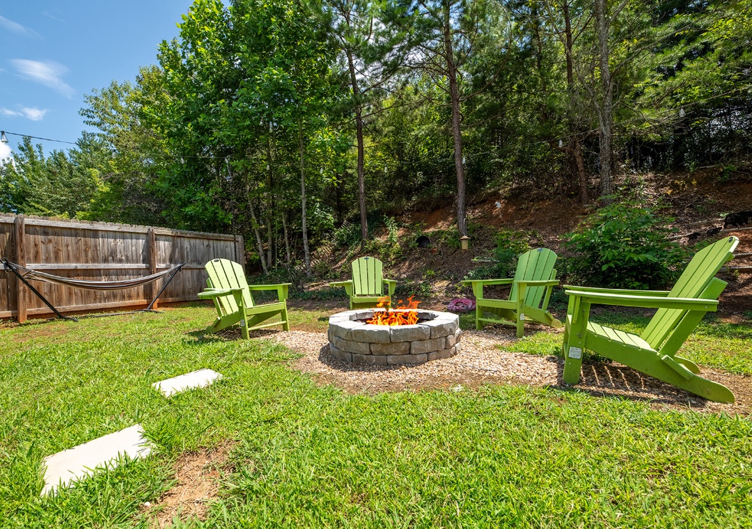 Gather around the fire pit in your private backyard, surrounded by lush trees and vibrant green seating. Perfect for evening s'mores and unwinding under the stars.