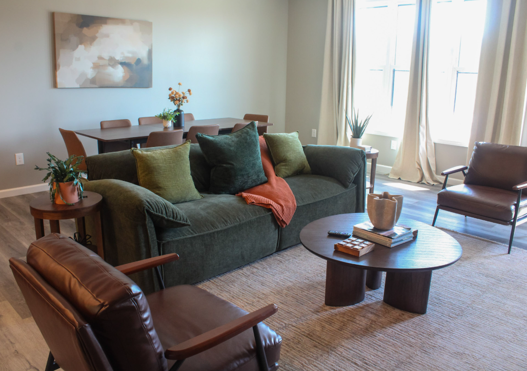 Relax into your own stylish living space, where a plush sofa, sleek leather chairs, and warm wood accents invite you to unwind, while the open dining area and sunlit windows create a welcoming atmosphere for every moment of your stay.