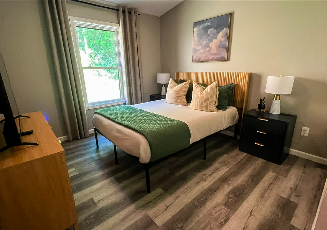 Your peaceful bedroom features a plush bed with fresh linens, warm natural light from the window, and modern touches like a flat-screen TV—perfect for unwinding after exploring.