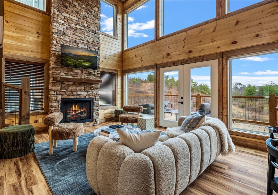 Sink into plush seating by your crackling fireplace, where soaring windows frame peaceful views and warm wood embraces you in comfort.