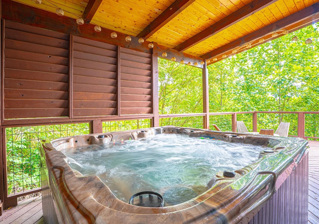 Soak away your cares in your private hot tub, surrounded by lush forest views from the comfort of a covered deck with rustic wood ceiling and twinkling lights overhead.