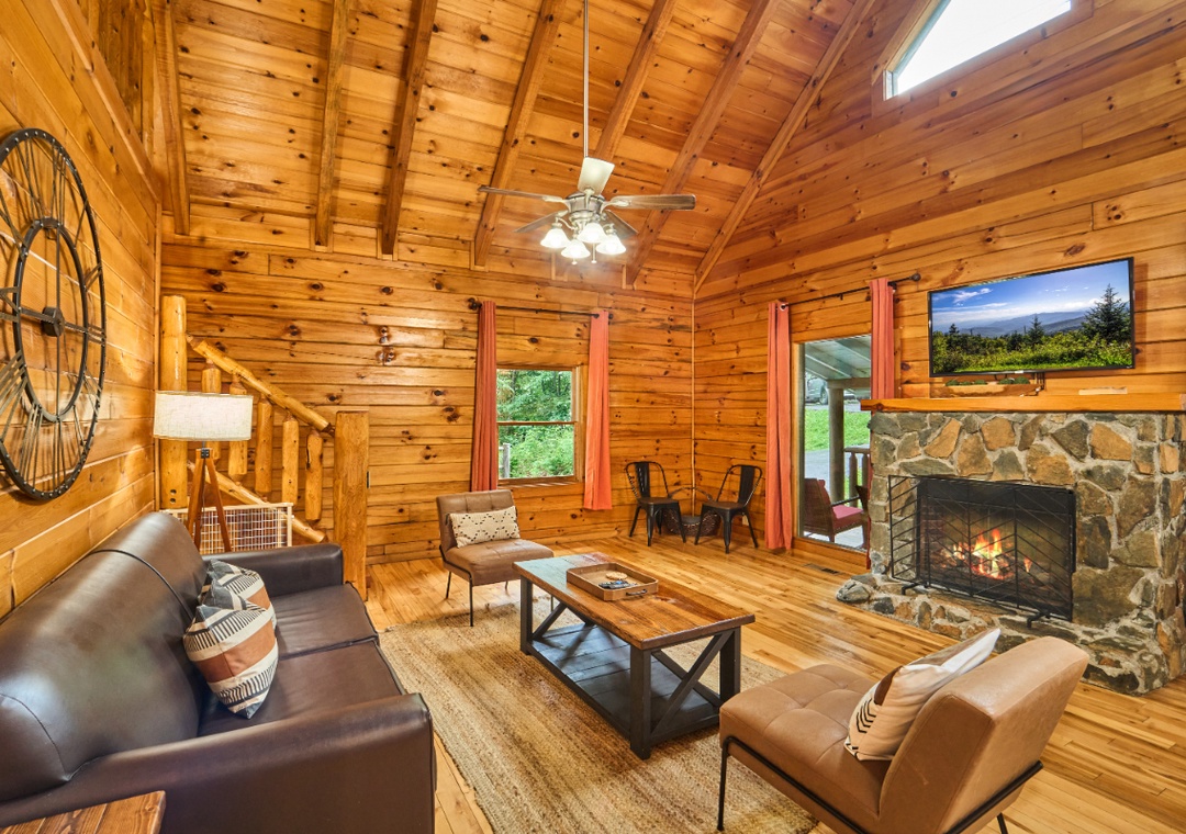 Relax in your inviting living room with a crackling stone fireplace, soaring cathedral ceilings, and mountain views visible through the windows. Unwind on comfortable leather seating while natural wood surrounds you in warmth.