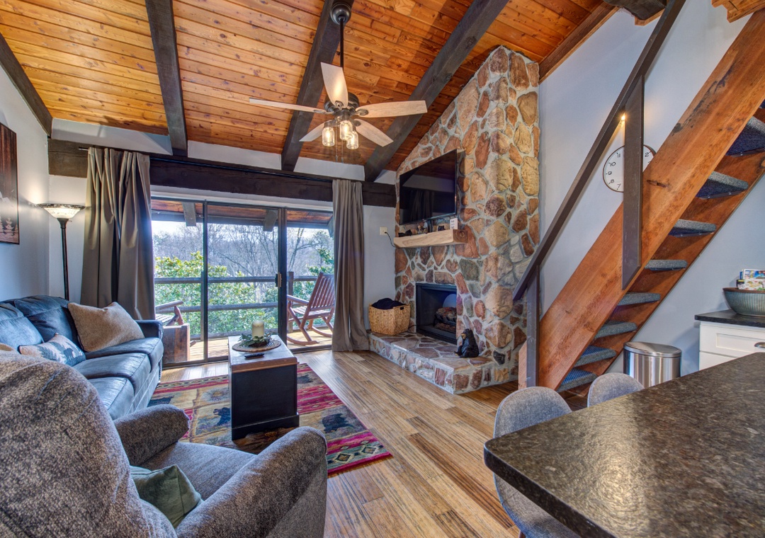 Relax in your rustic living room with stone fireplace, exposed beams, and private balcony overlooking nature.