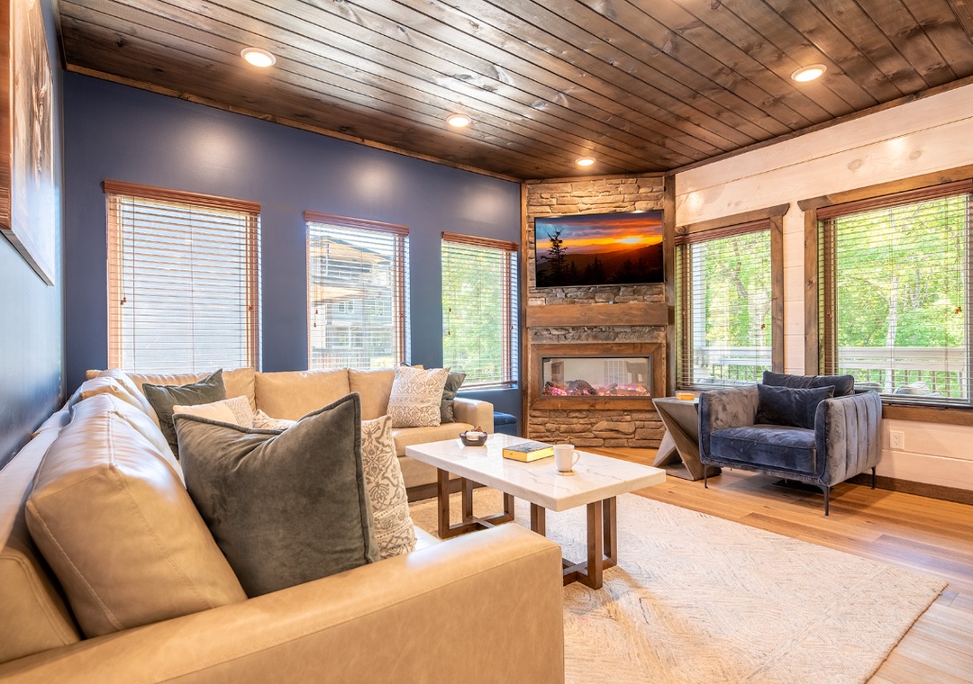 Sink into plush seating and let your worries fade as you gaze at lush greenery through large windows, while the cozy fireplace creates a warm, inviting glow perfect for relaxation.