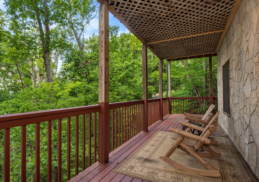 Settle into your private deck surrounded by lush forest canopy. Rock gently in rustic wooden chairs as sunlight filters through vibrant green leaves, creating your peaceful woodland retreat.