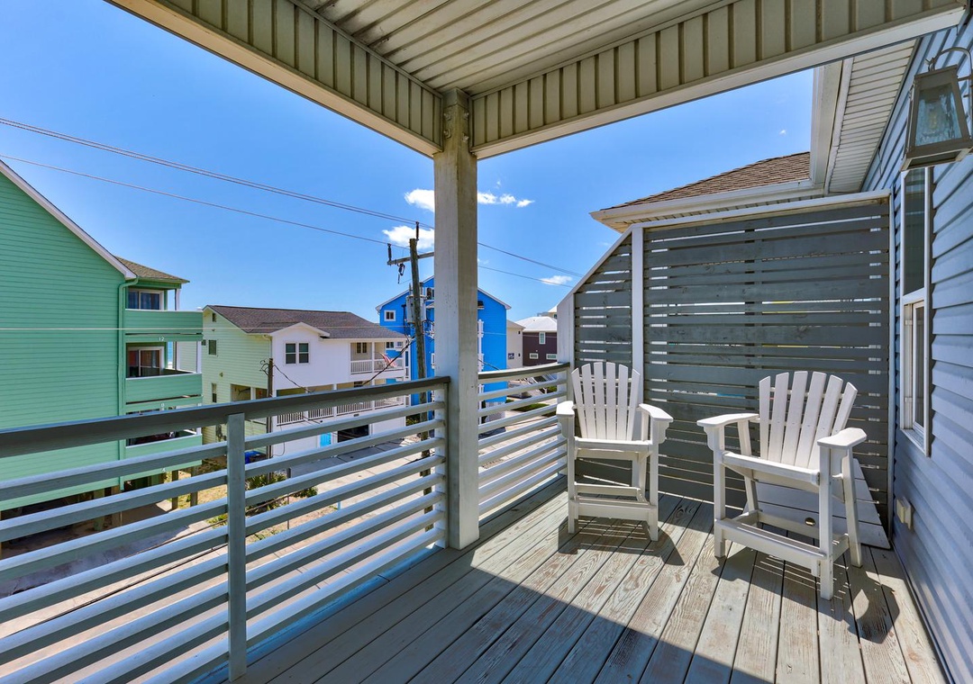 Your private balcony awaits with Adirondack chairs perfect for morning coffee or evening relaxation, framed by charming neighborhood views and coastal breezes overhead.
