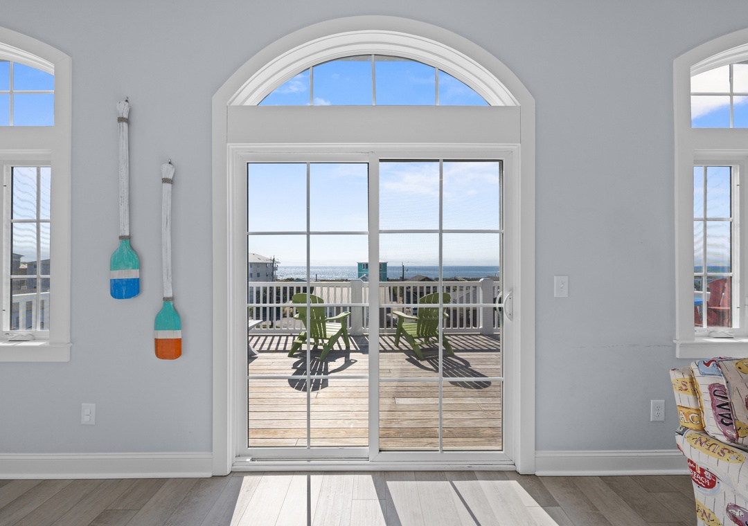 Sunlight streams through arched windows framing your private deck with ocean views. Coastal decor and bright, airy living space invite you to unwind in beach-house comfort.